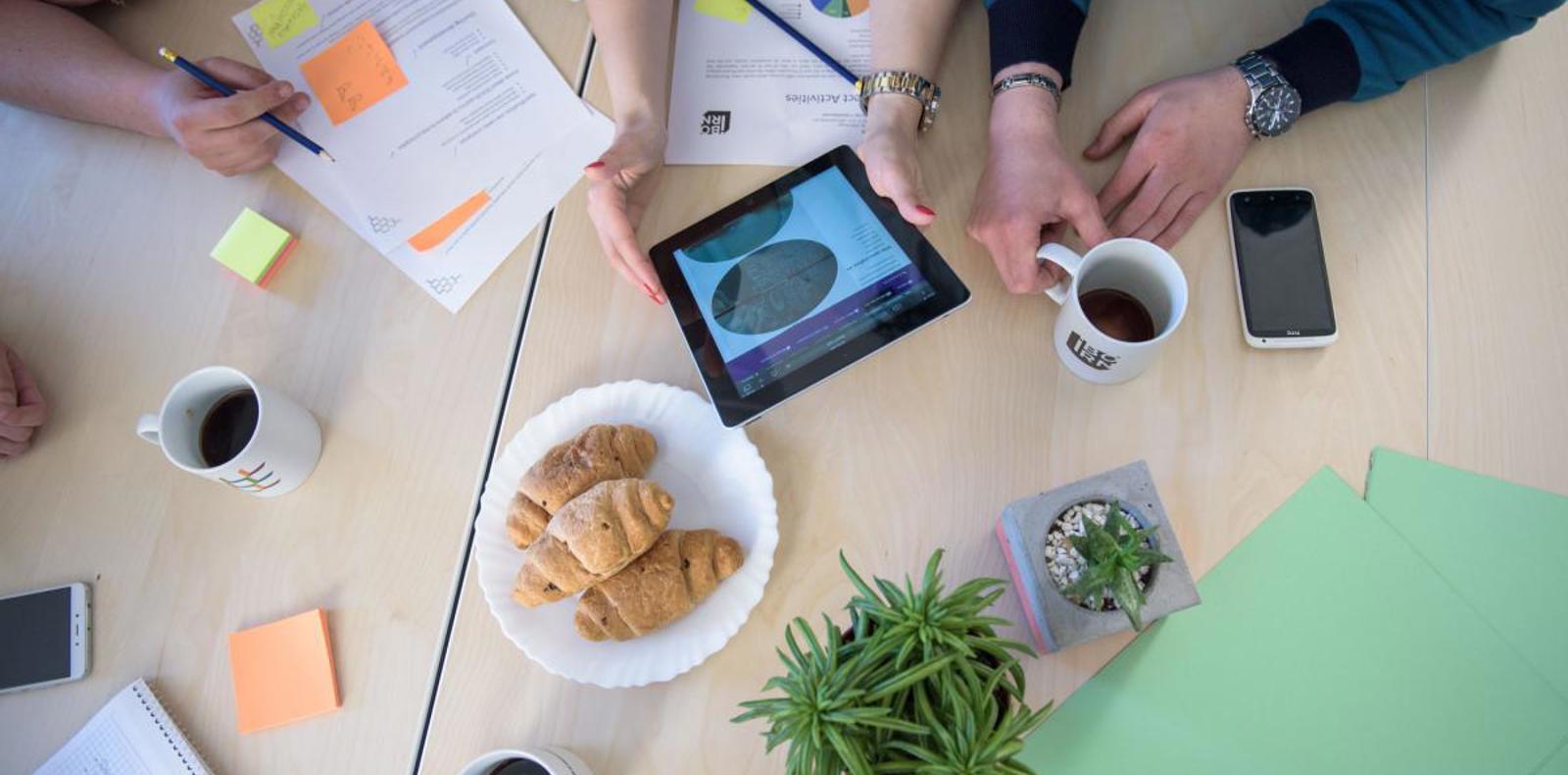 People gathered around table with tablet and coffee.