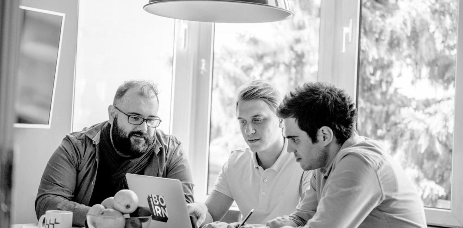 Three men working on laptops at a table, engrossed in their tasks.