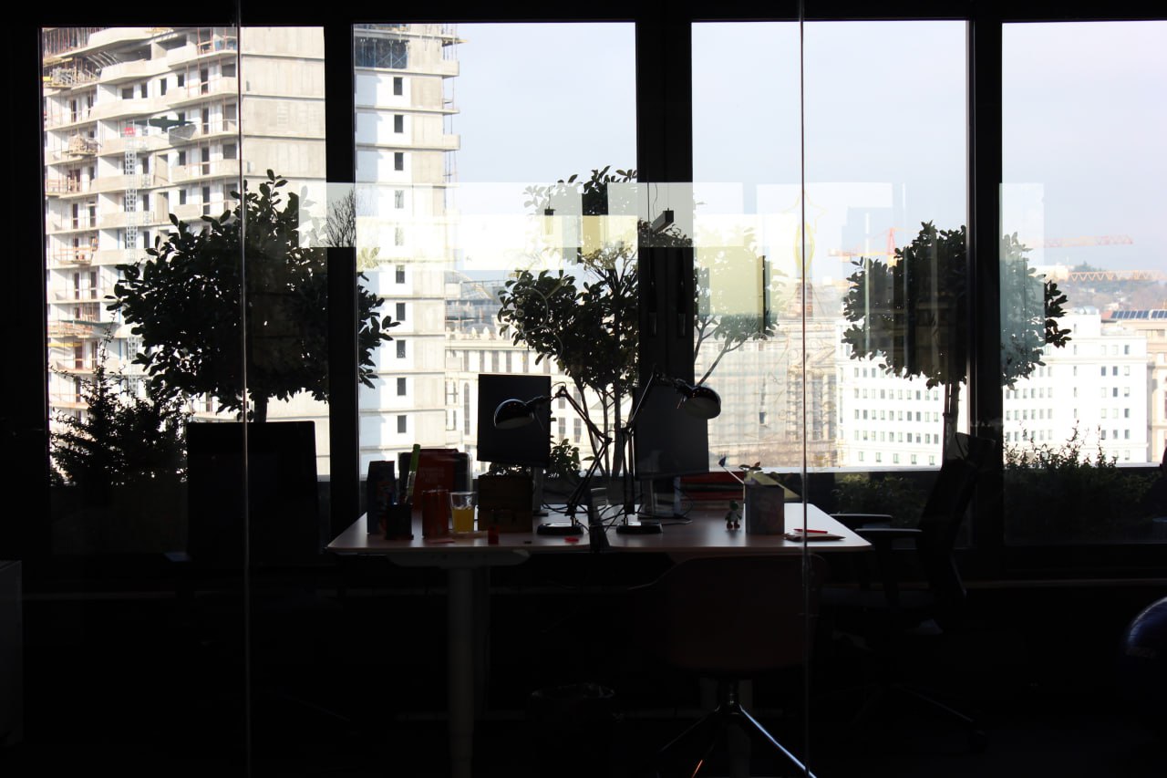 Two working desks placed in front of a window with a view of the cityscape, showcasing urban buildings.