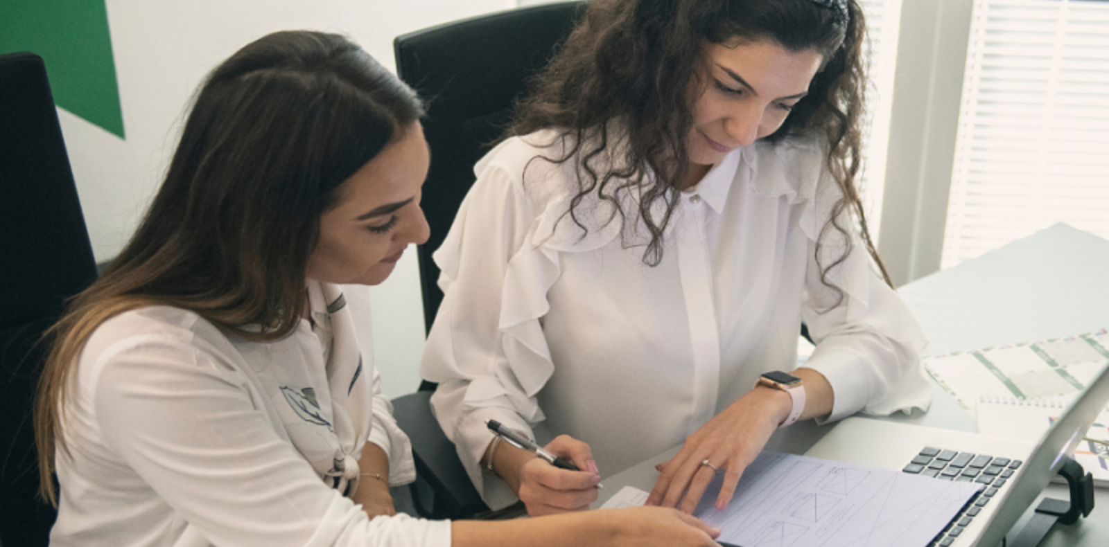 Two women focused on wireframes at a desk, collaborating and diligently working together.