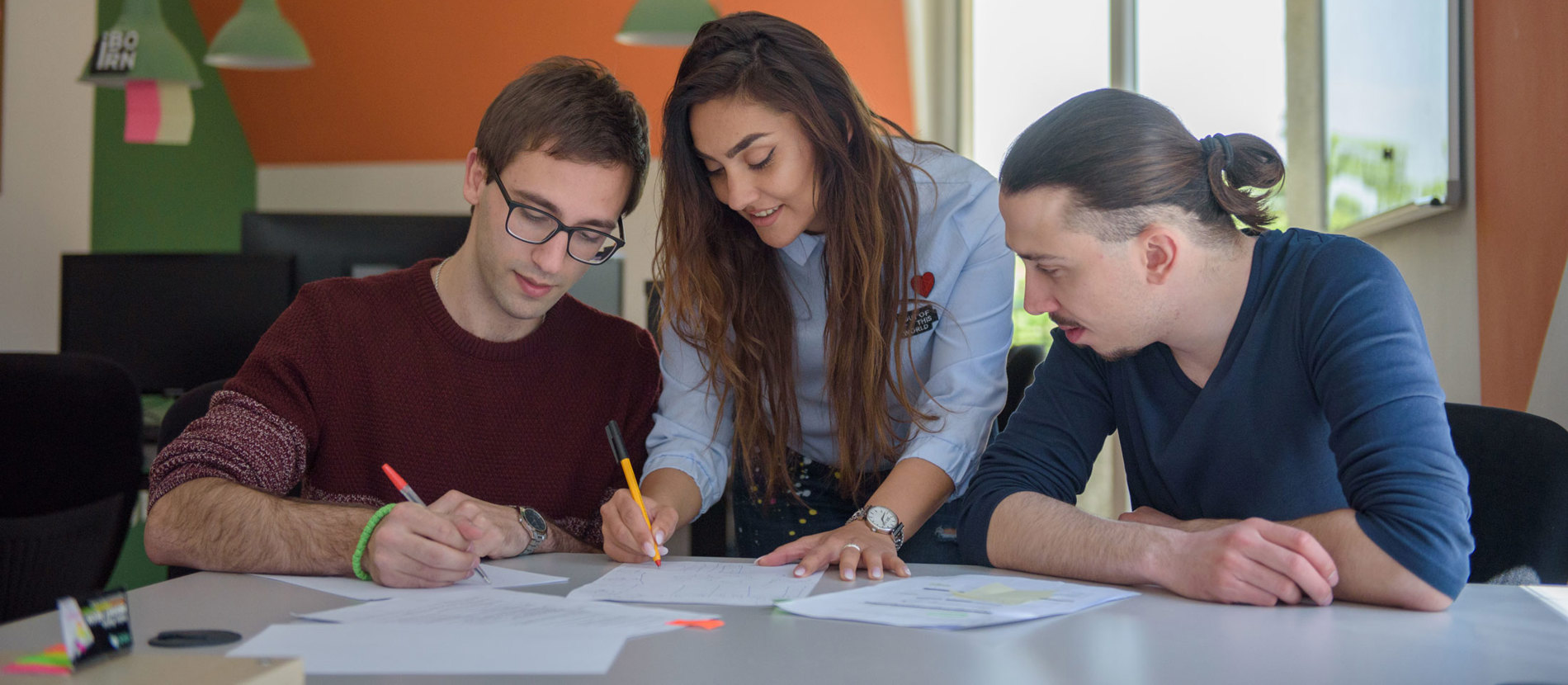 Three people collaborating at a table, focused on a laptop.