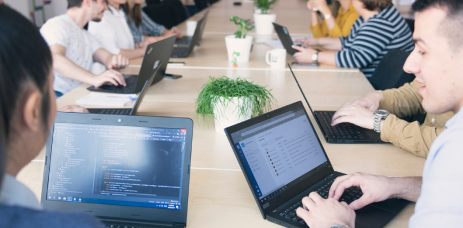 A diverse group of individuals sitting around a table, engrossed in their work on laptops.