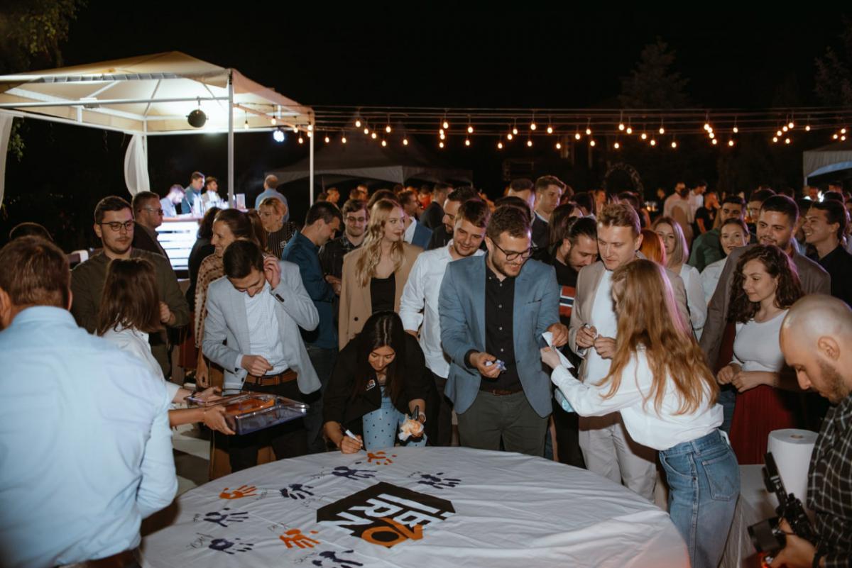 Employees at IBORN.NET gathered around, adding their signatures to a big canvas, symbolizing the mark they left at the company, the teamwork, and shared goals.