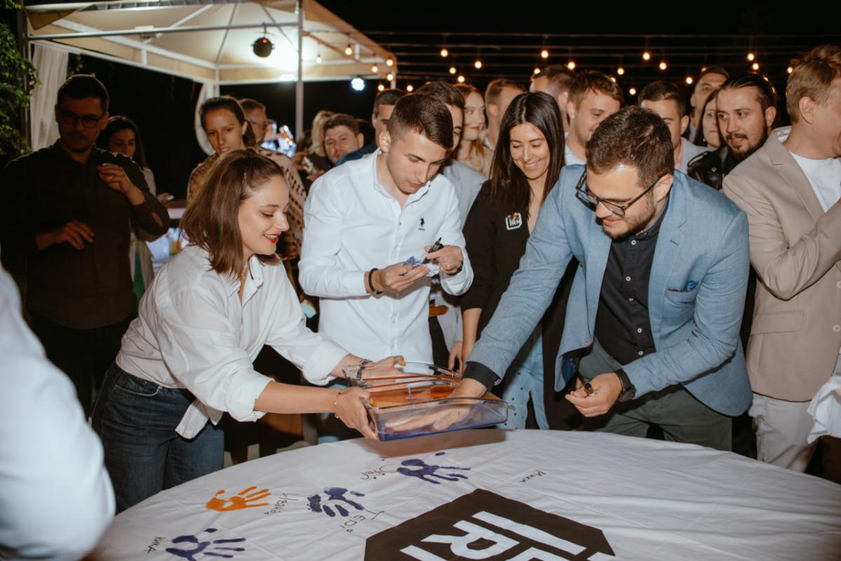 Employees at IBORN.NET gathered around, adding their signatures to a big canvas, symbolizing the mark they left at the company, the teamwork, and shared goals.