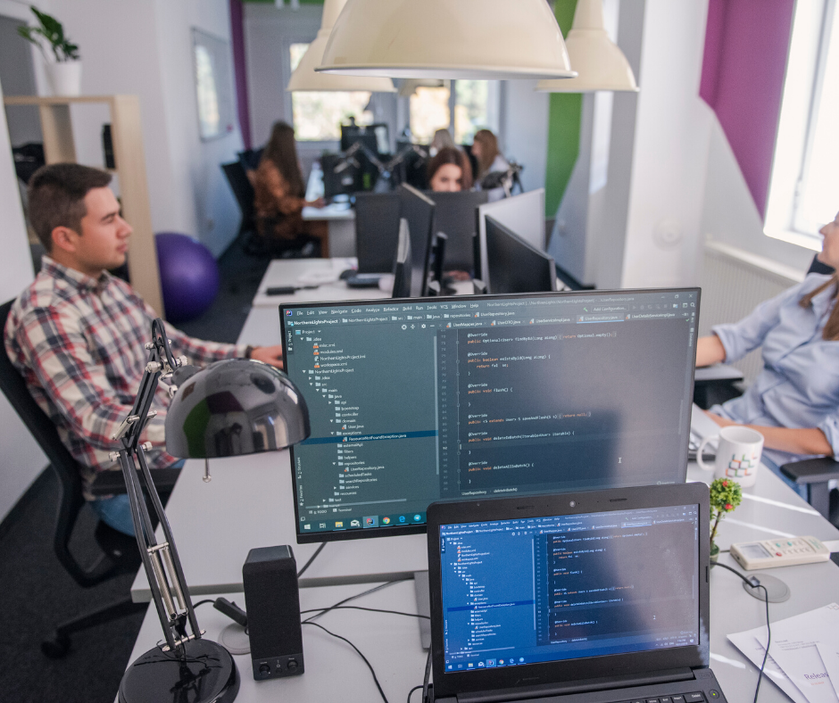 Developers working on their laptops and computers in a corporate office space.