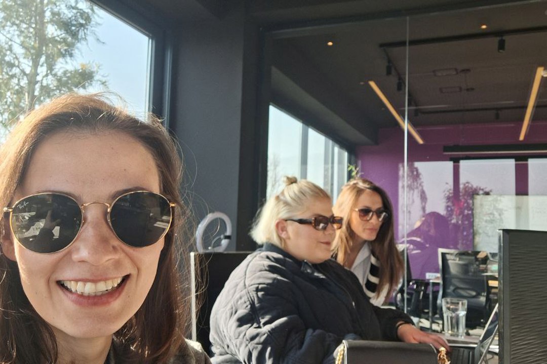 Three women wearing sunglasses, sitting at a table, working on a laptop together.