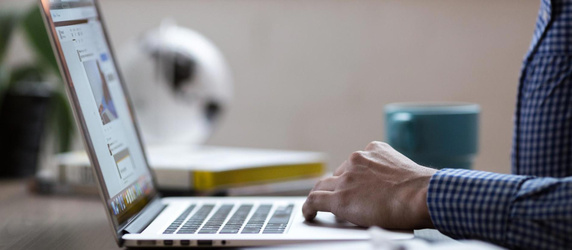 Laptop on a desk with a coffee mug, a small cactus, and a desk lamp.  