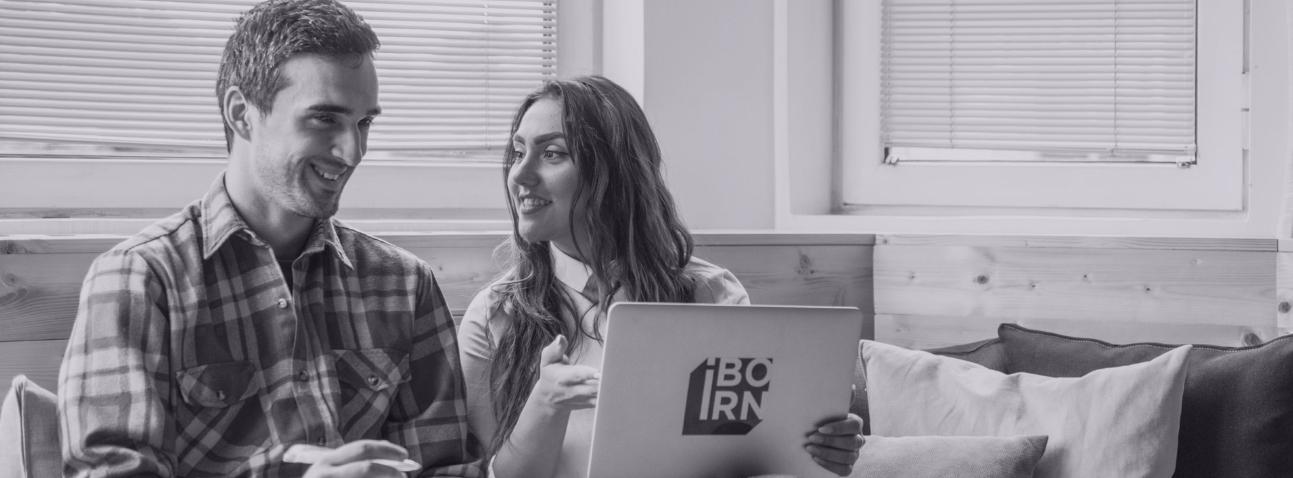 Two colleagues sitting on a couch, engrossed in their laptop, working together.