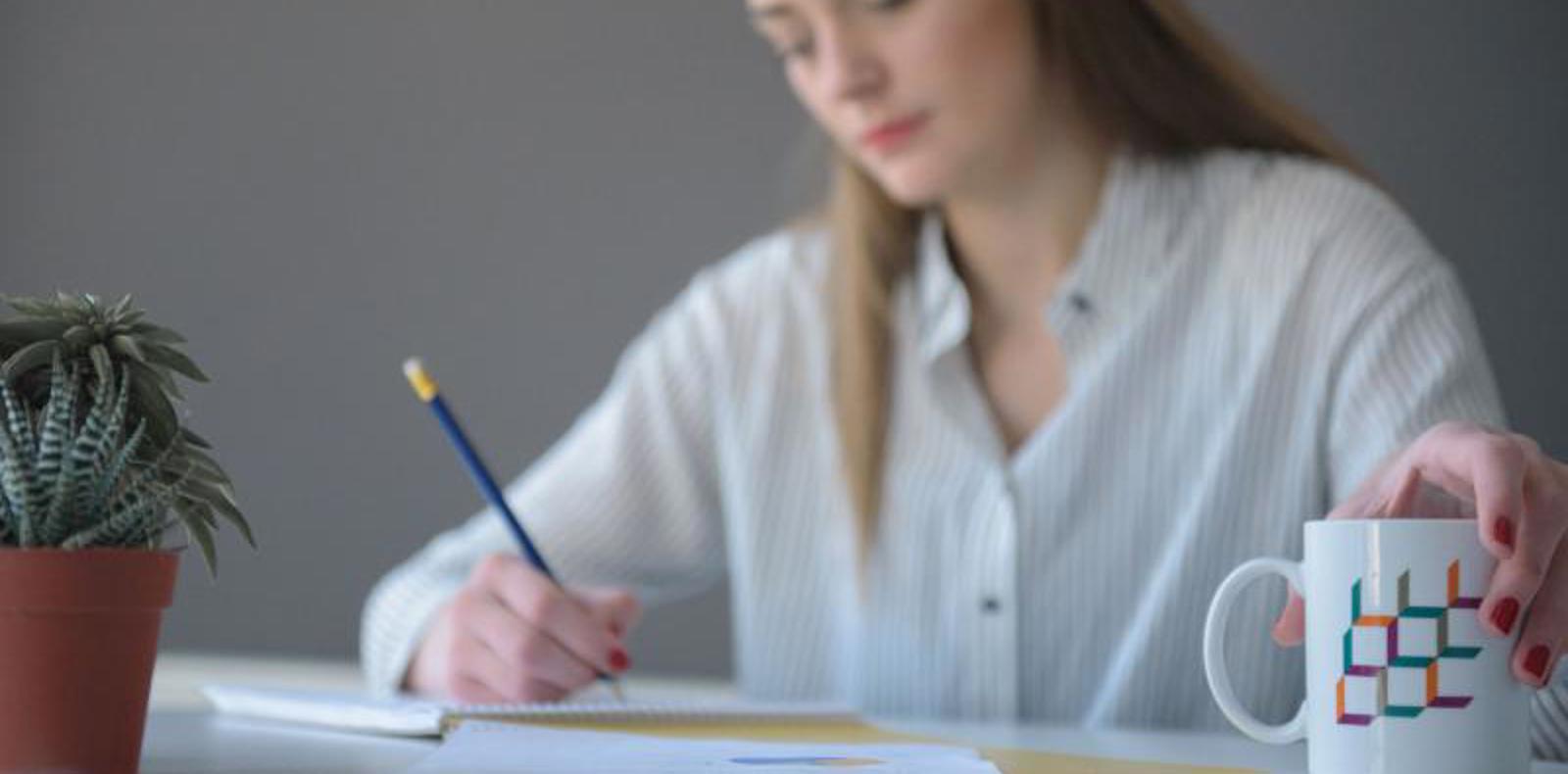 A woman writing something on a piece of paper and holding a mug.