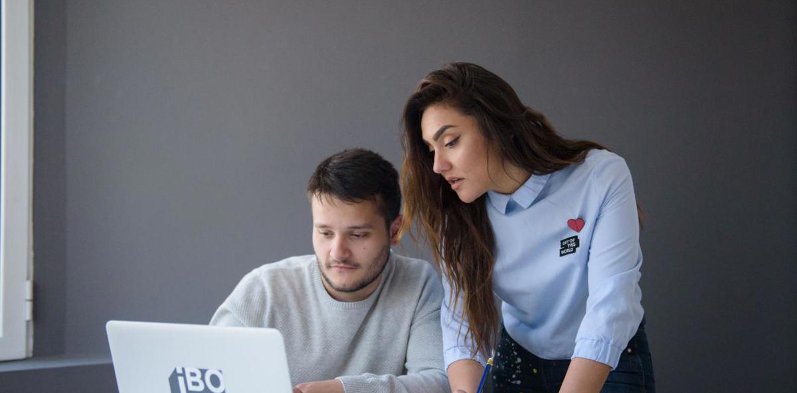 A man and woman collaborating on a laptop, engaged in focused work together.