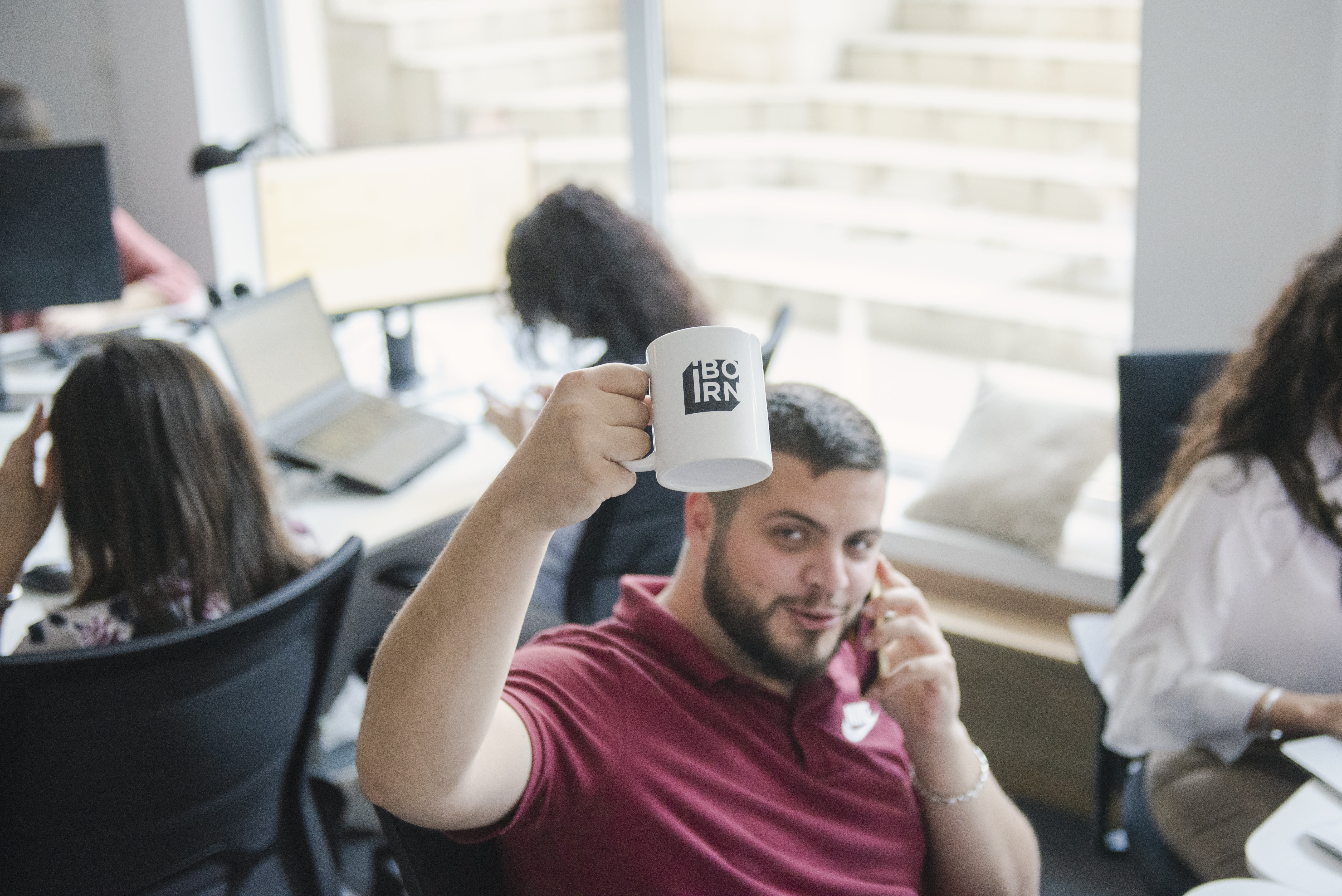 A person holding a mug with the IBORN logo on it and showing it to the camera.
