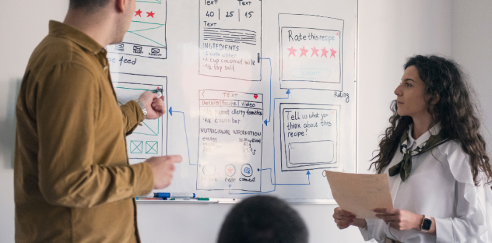 Developer and a designer standing in front of a whiteboard, discussing project wireframes.