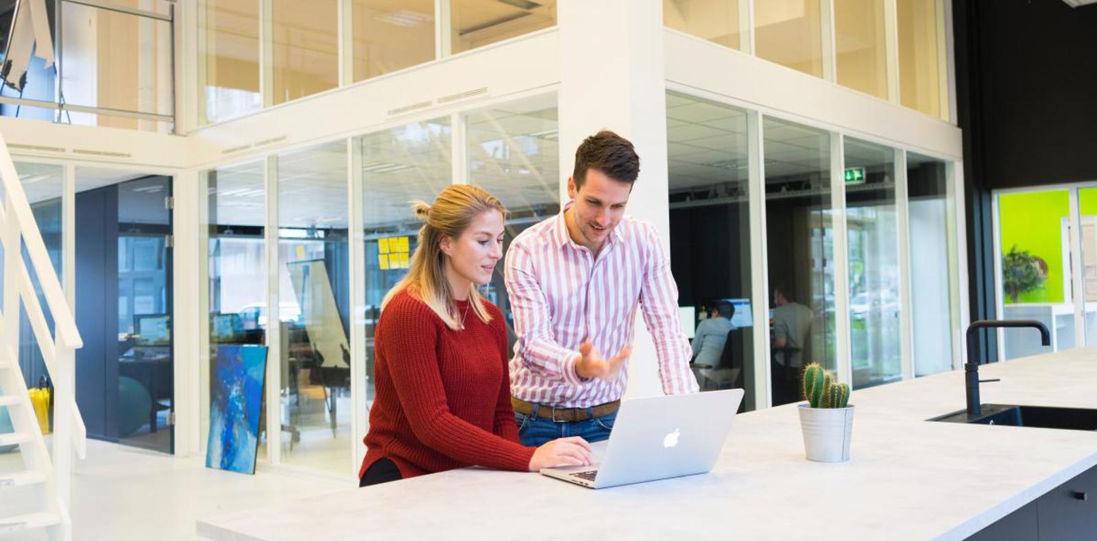 Two colleagues working together on a mac in a modern office environment.