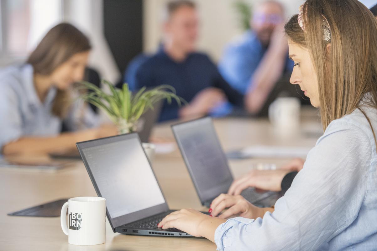 Image of a woman using a laptop surrounded by people.