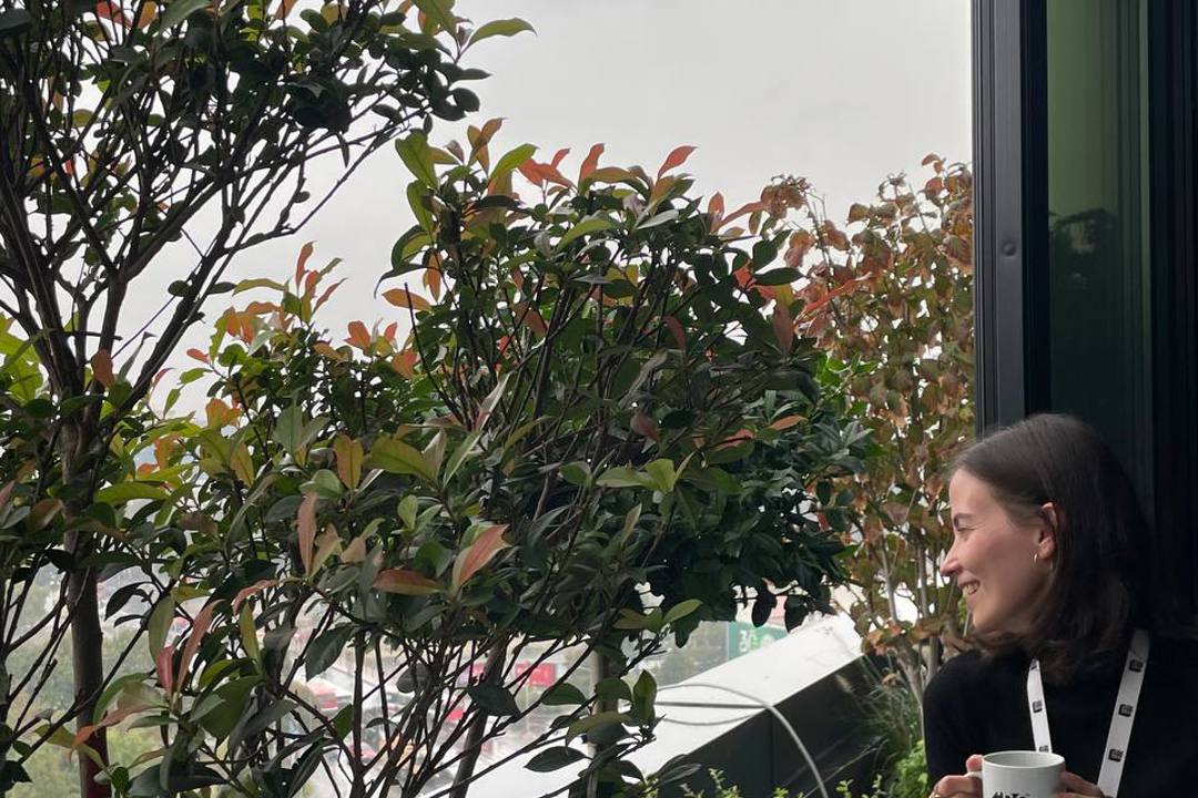 Woman enjoying morning coffee in a IBORN mug on balcony overlooking cityscape.