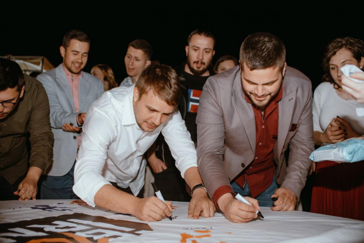 Employees at IBORN.NET gathered around, adding their signatures to a big canvas, symbolizing the mark they left at the company, the teamwork, and shared goals.