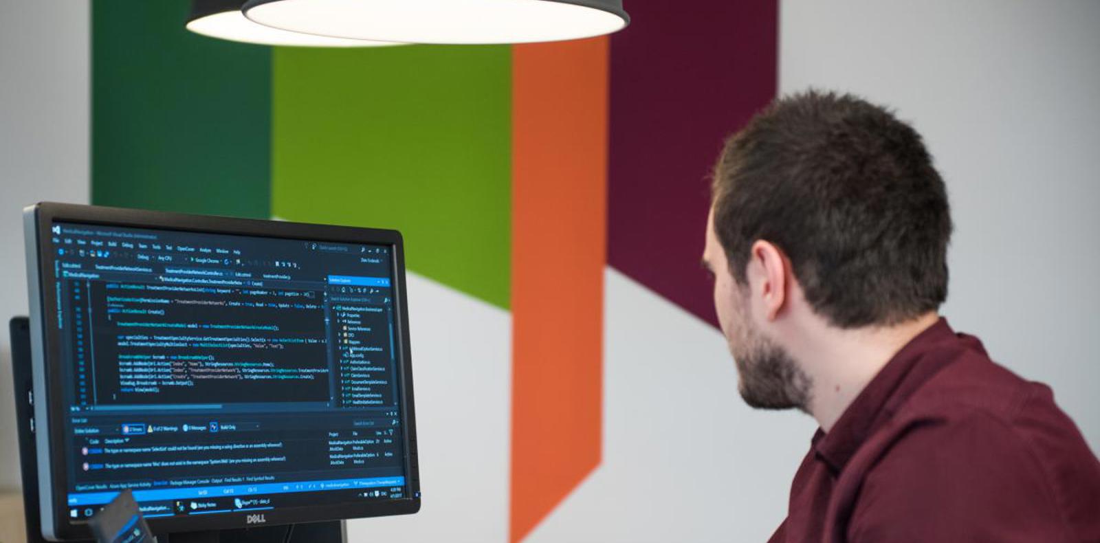 A man sitting at a desk, focused on a computer screen, working diligently.