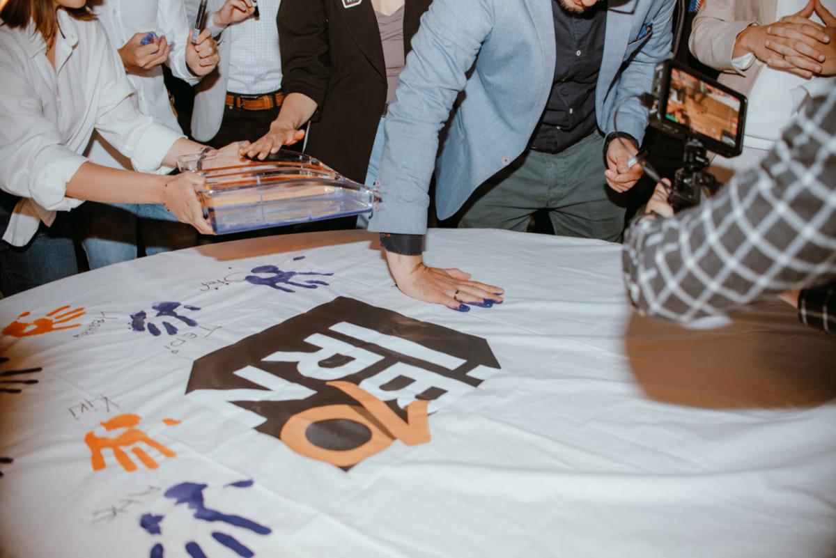 Employees at IBORN.NET gathered around, adding their signatures to a big canvas, symbolizing the mark they left at the company, the teamwork, and shared goals.