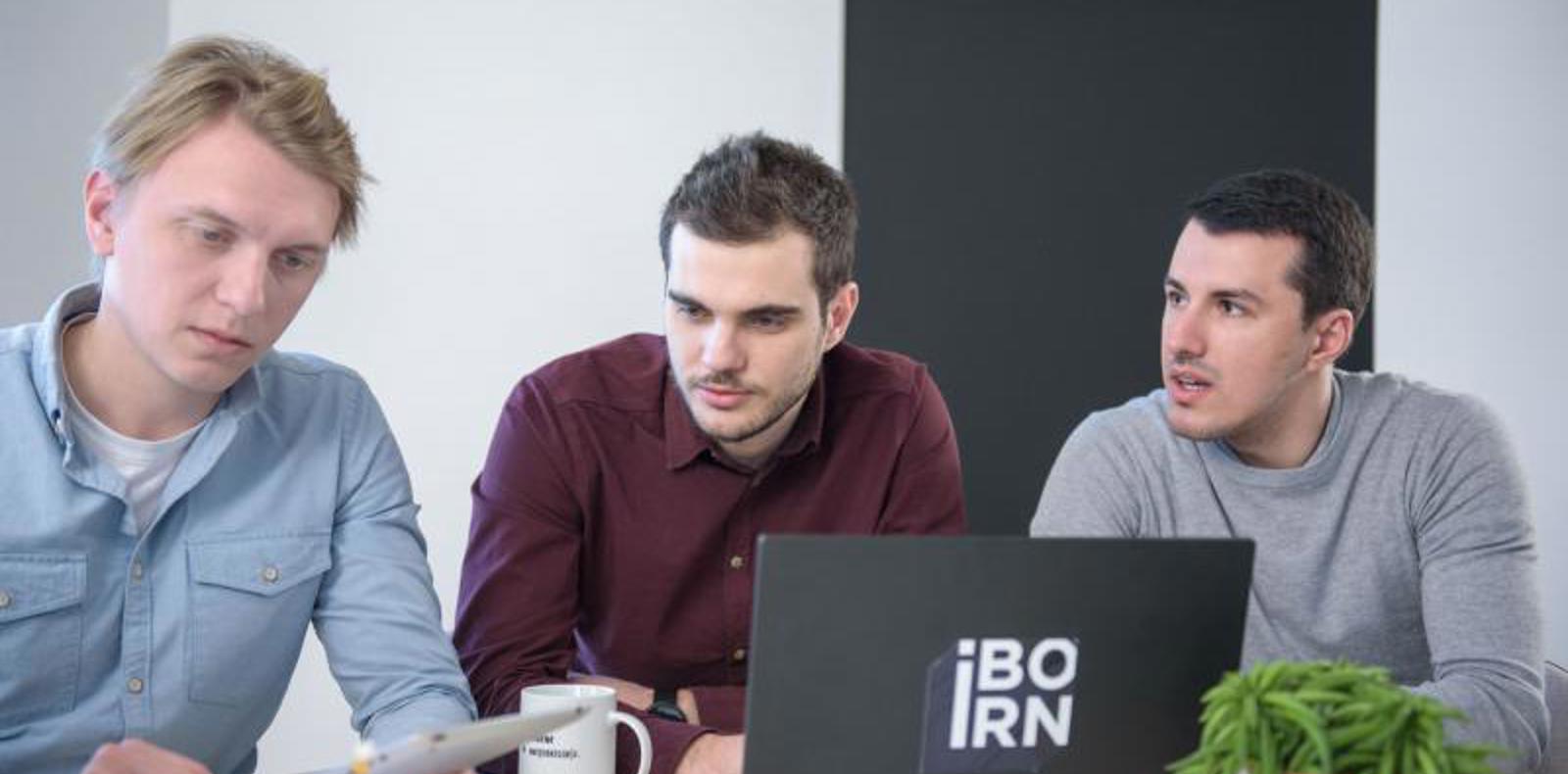 Three software engineers working together on a laptop in bright conference room.