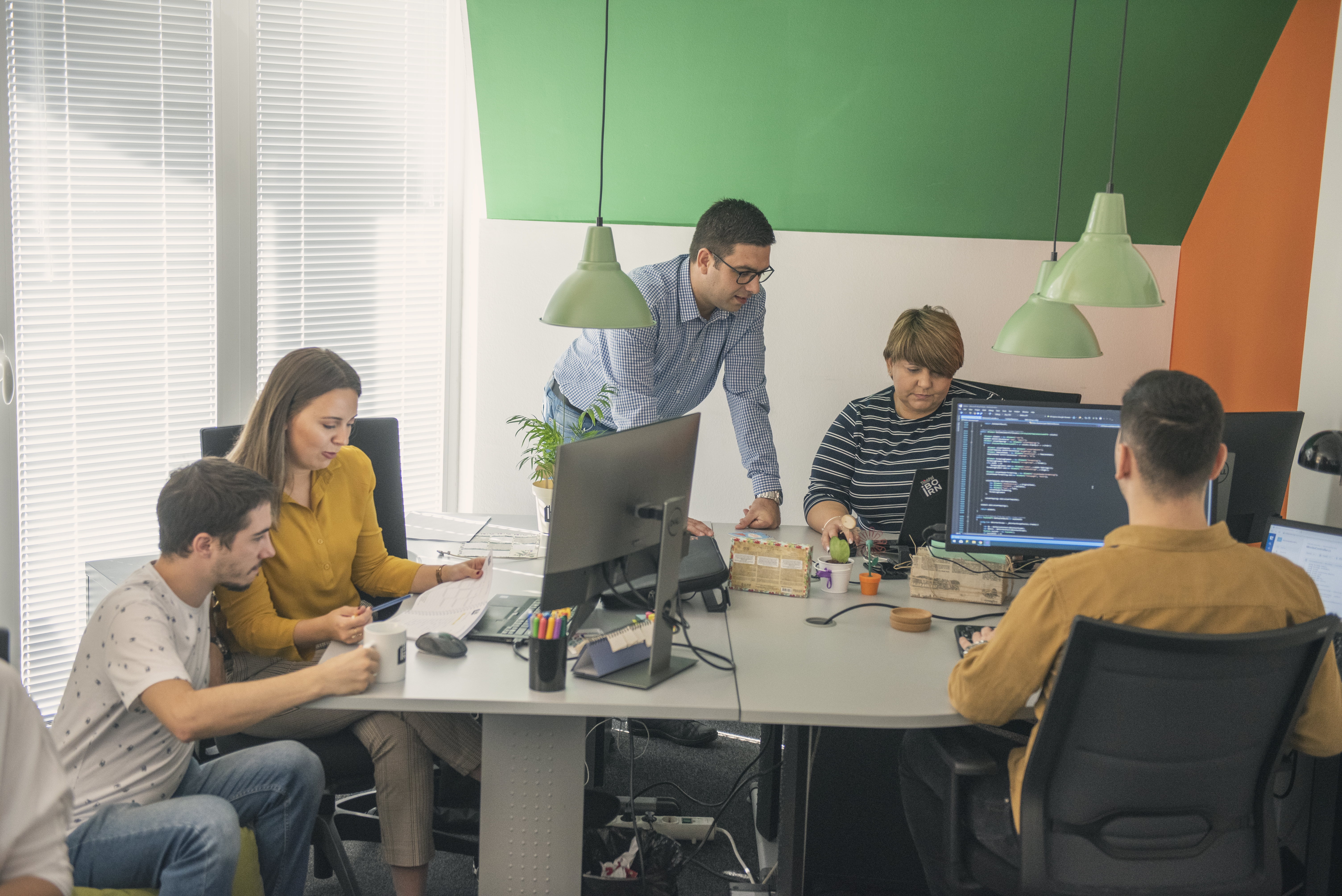 Software engineers sitting at desks, focused on their computer screens in a busy workspace.