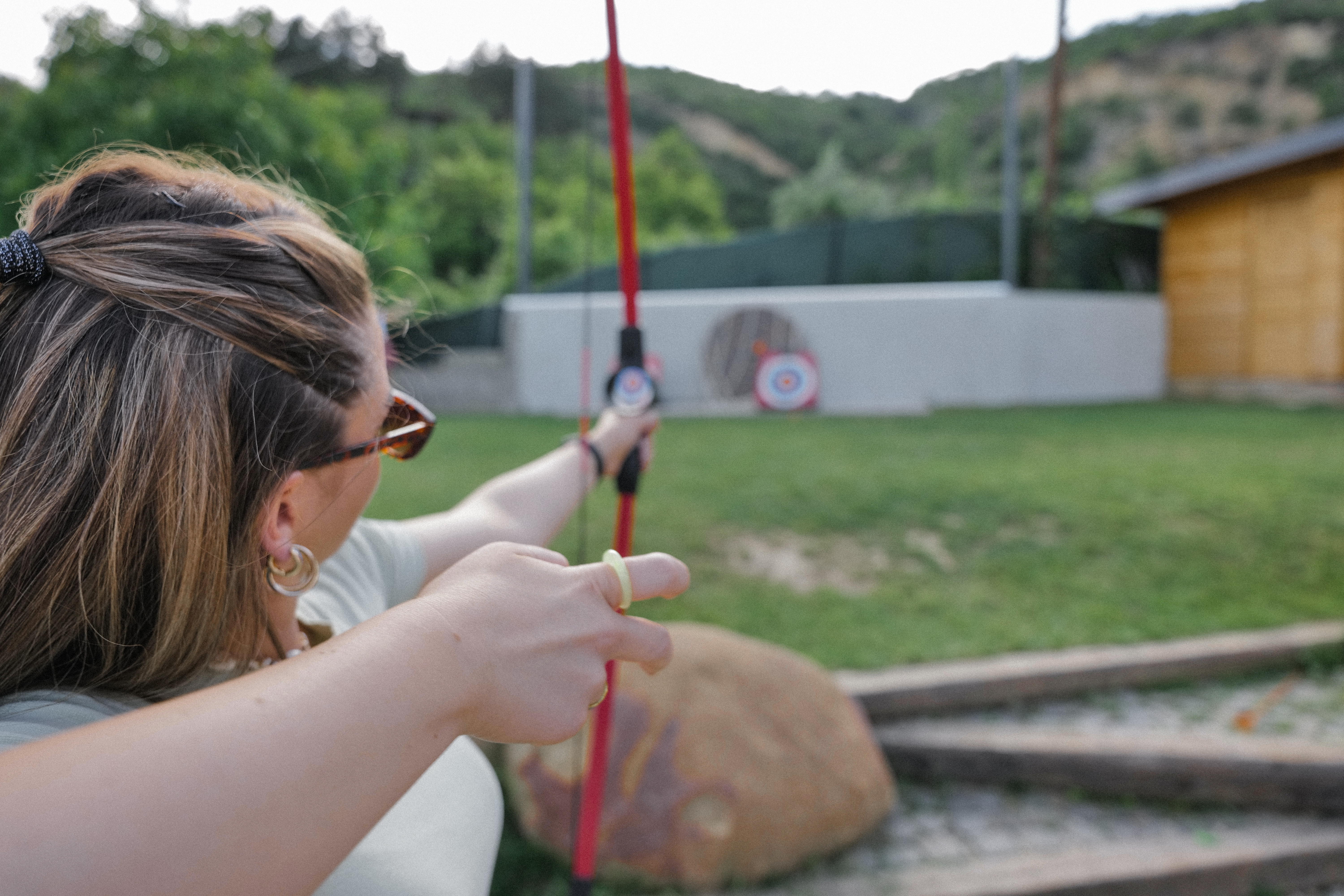 A woman focuses intently as she aims her bow at a target in the distance.