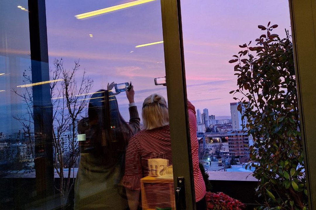 Two people standing outside, taking a picture of the beautiful sky. 