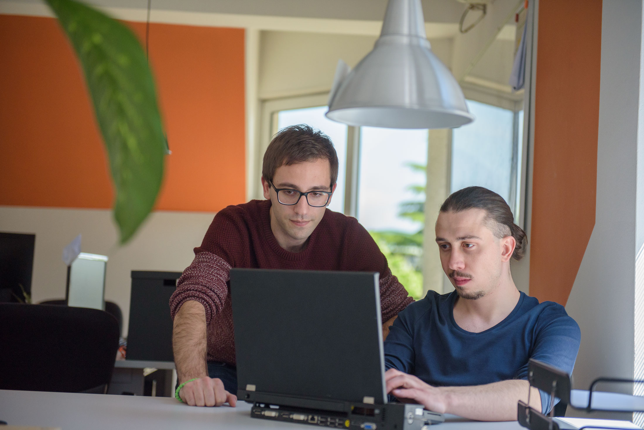 Two men working on laptop in an office setting.