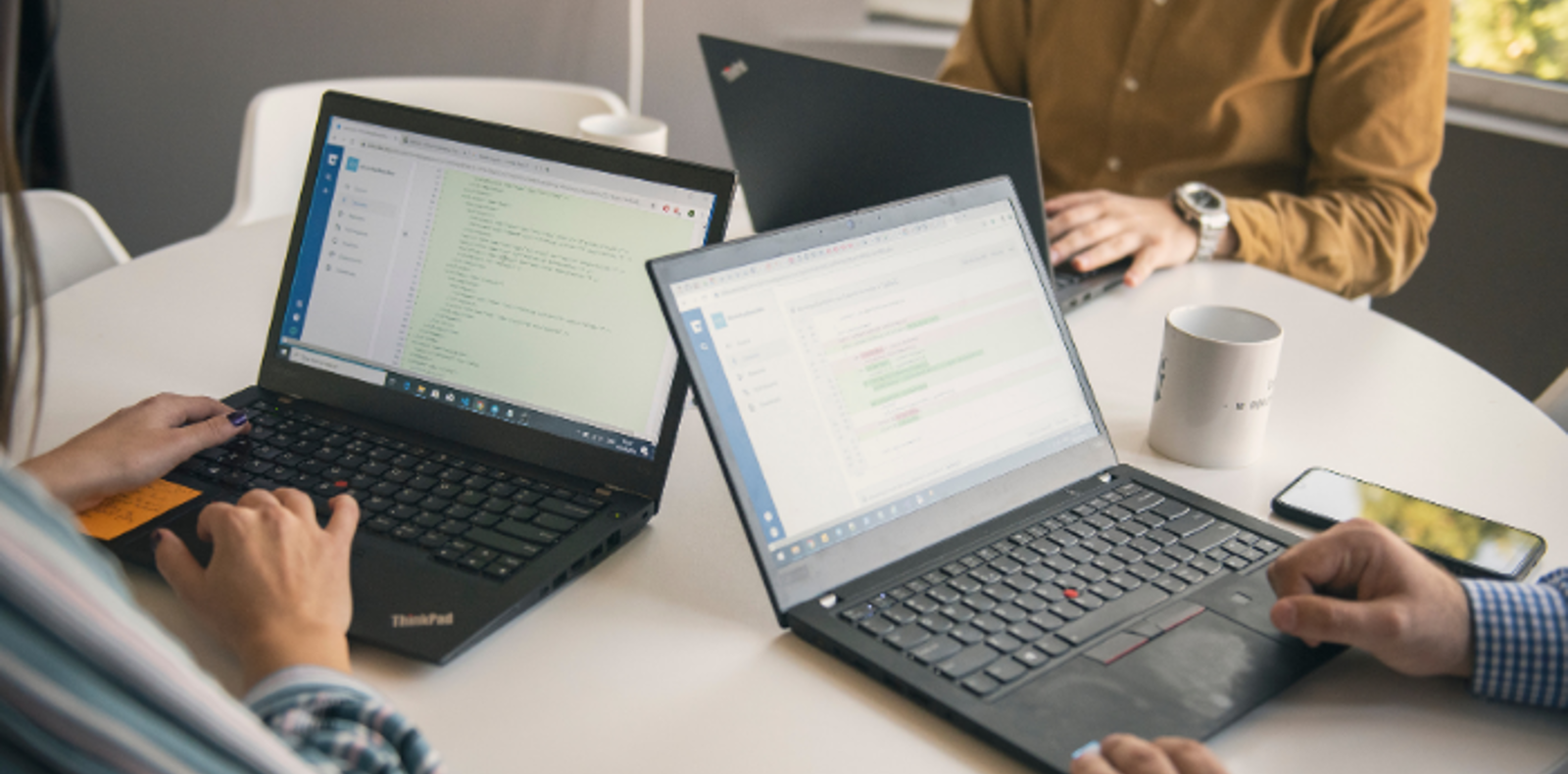 Three  individuals focused on their laptops, working diligently at a table in a professional setting