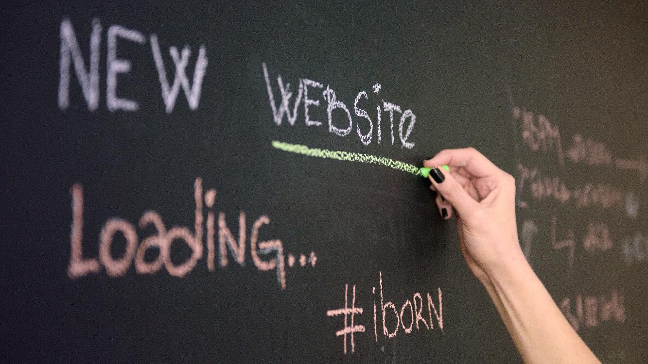 Person writing on a black board "New Website".